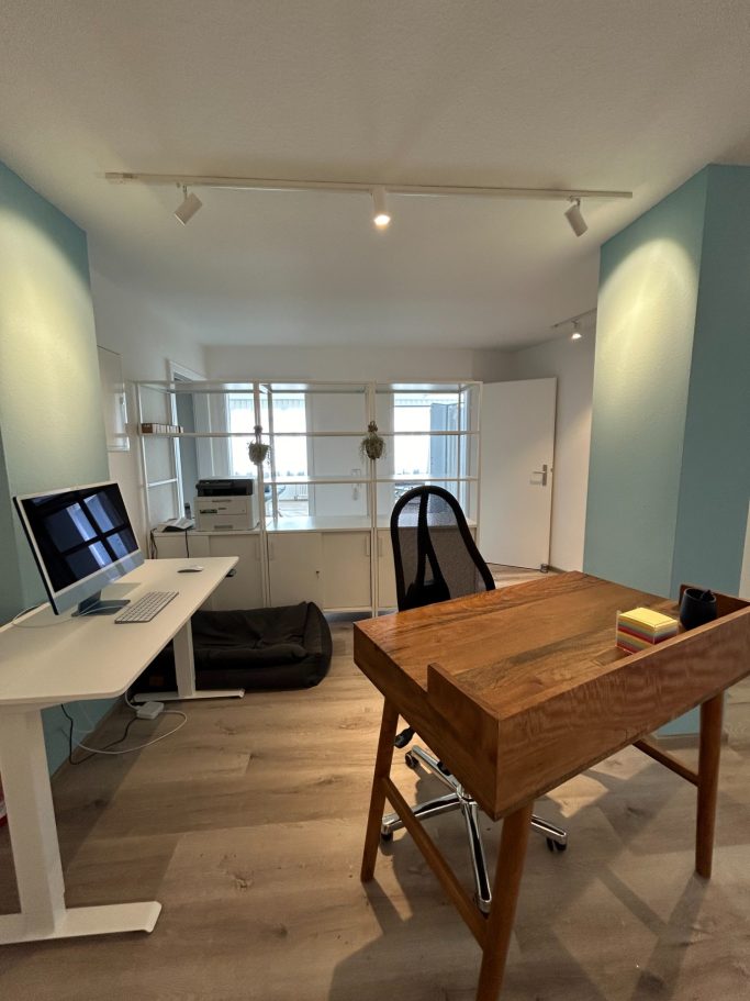 Helles Büro mit Schreibtisch, Computer und einem großen Fenster.