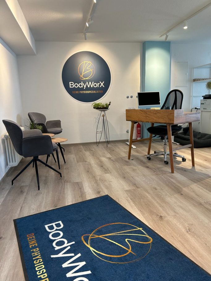 Modern Büroraum mit Stühlen, Tisch, Computer und BodyWorx-Logo auf dem Boden.