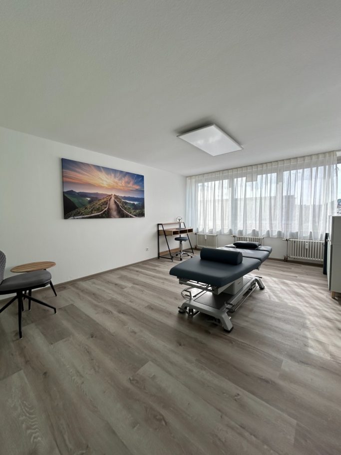 Heller, moderner Behandlungsraum mit Holzboden und großem Fenster.