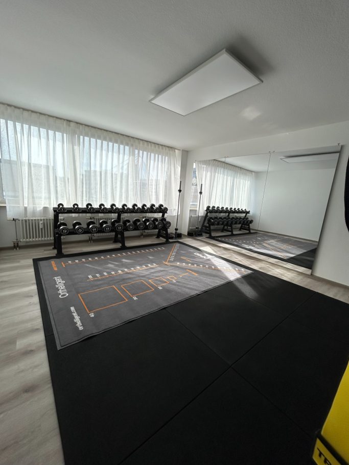 Klarer Fitnessraum mit Gewichten, Spiegel und hellem Licht.
