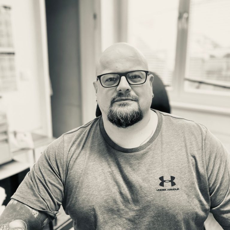 Ein Mann mit Brille und glattem Kopf sitzt an einem Schreibtisch in einem Büro.