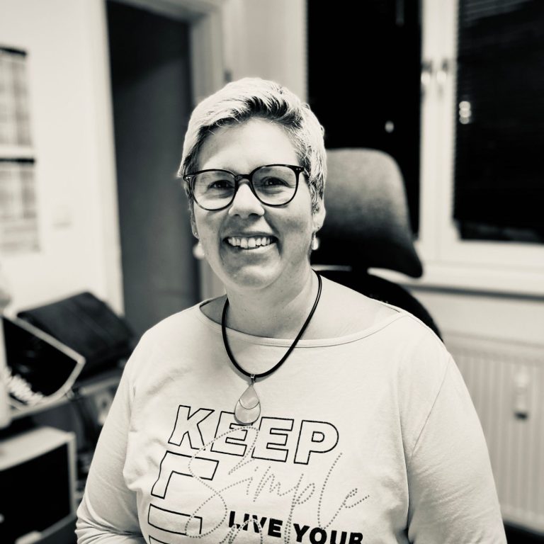 Lächelnde Person mit Brille in einem modernen Büro.